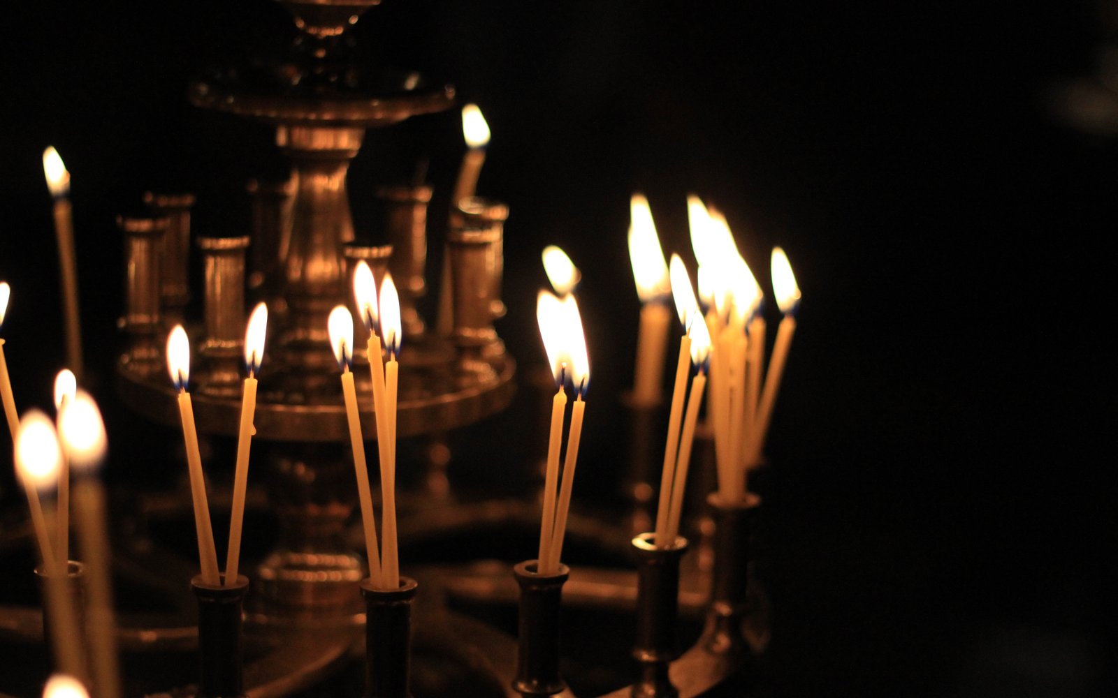 Lit beeswax candles on a brass candle stand in a darkened Orthodox church